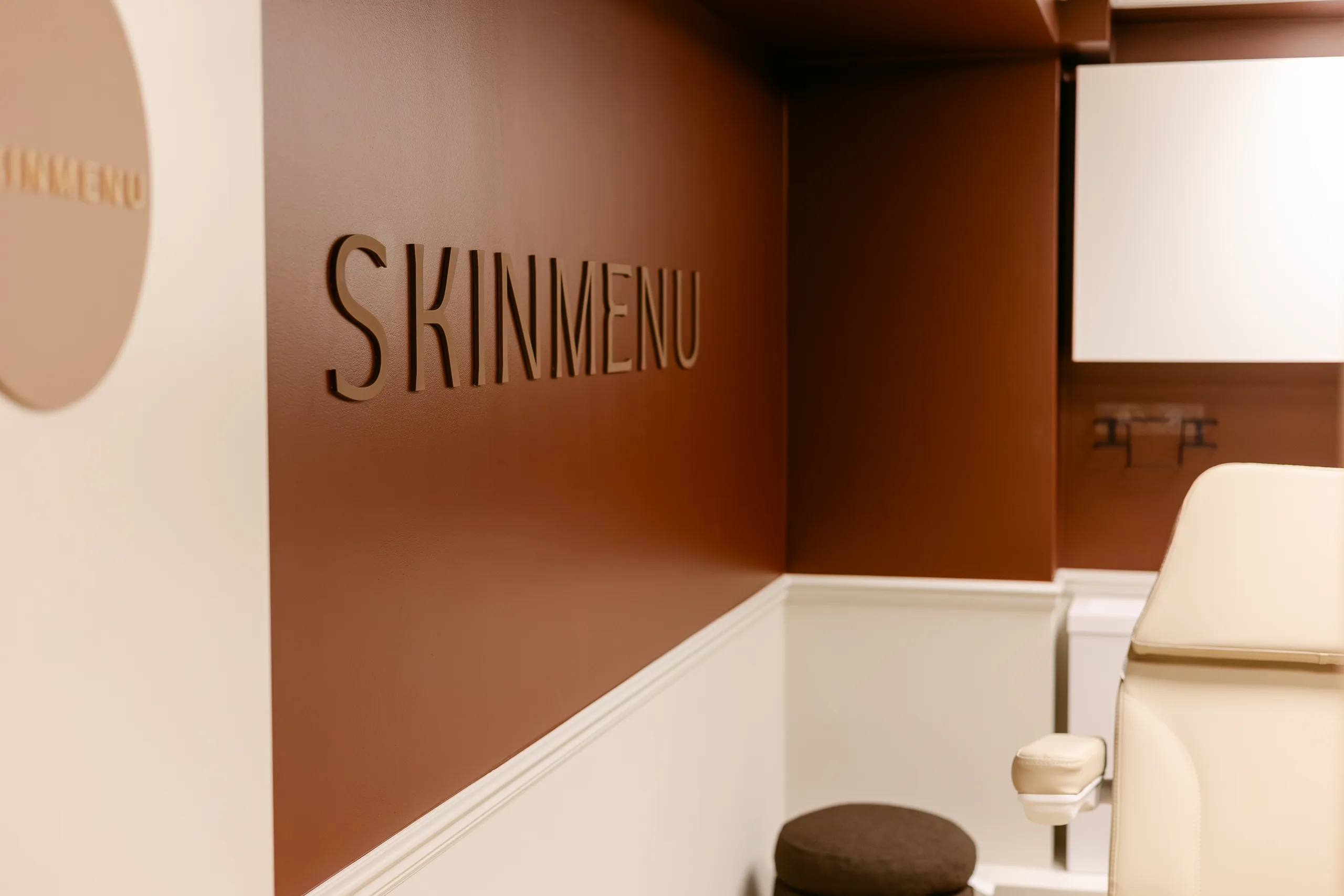 The SKINMENU treatment room, with the clinic wordmark on a burgundy wall